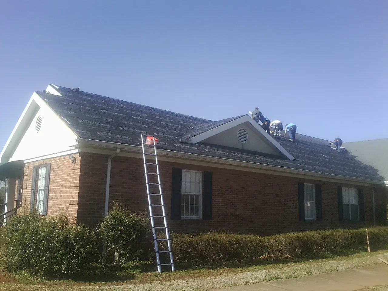 Crew tearing shingles off a brick ranch roof with a ladder set — Metal Roof Repair work by our crew in Kremmling