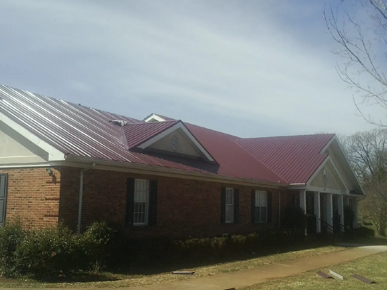 Red metal roof with gabled entries on a long brick building, from a Hail Damage Roof Repair job in Kremmling
