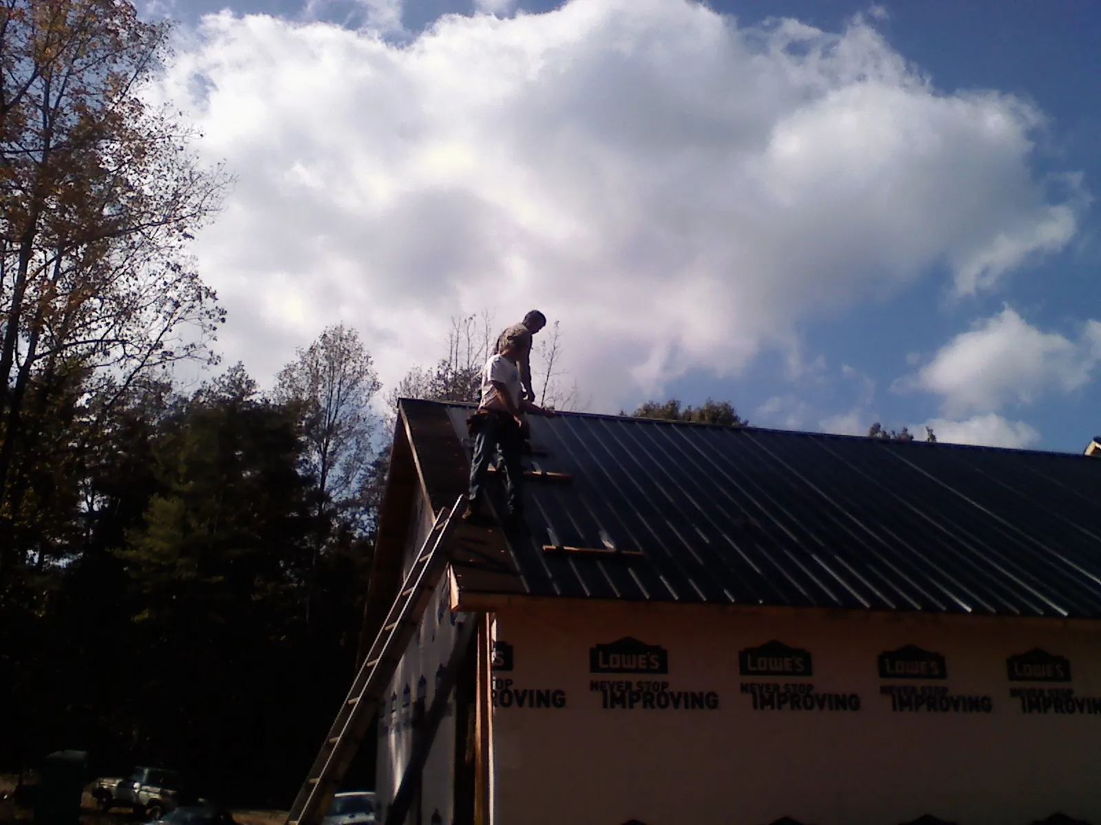 Roofer fastening dark metal panels high against a cloudy sky, from a Roof Inspection job in Kremmling